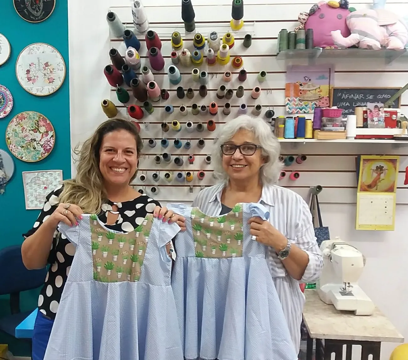 Duas alunas do ateliê exibindo as batas de algodão que modelaram e costuraram