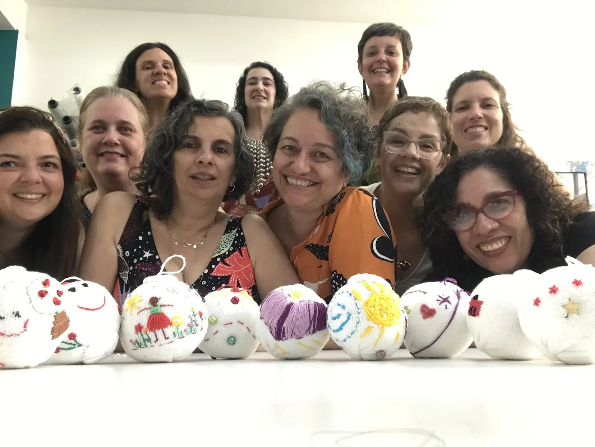 Grupo de mulheres sorrindo atrás de uma fileira de bolas de tecido que bordaram no ateliê